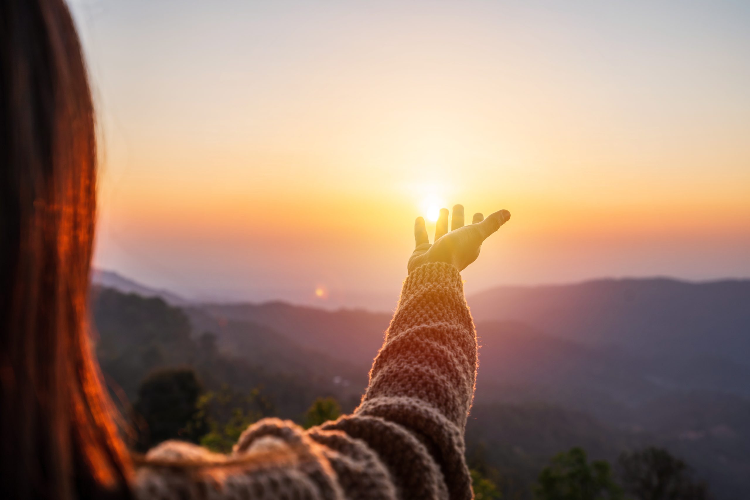 Femme levant la main vers le soleil